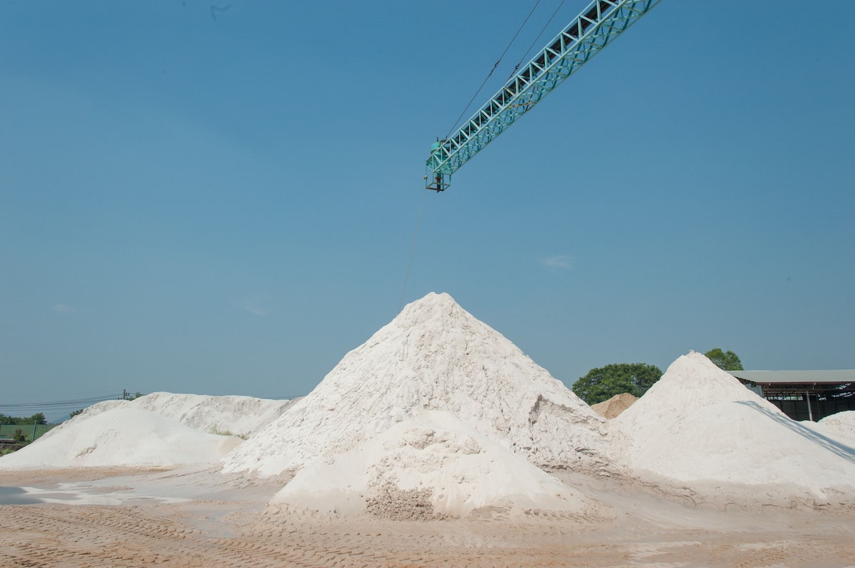 Three large piles of silica sand under blue sky.