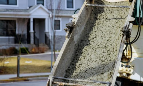 Close-up of a construction chute pouring stucco in front of a residential building