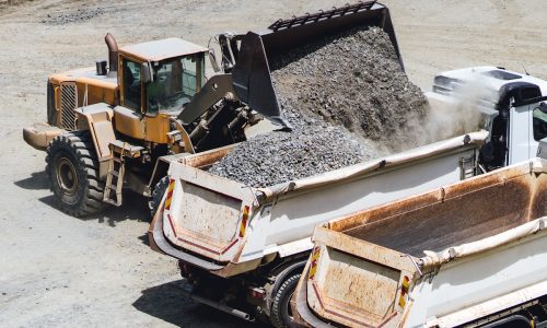 A yellow front loader transferring crushed aggregate into a dump truck at a construction site.