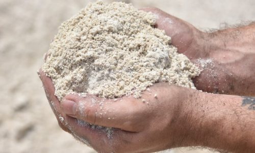 A man holding construction sand in his palm, emphasizing its fine texture and suitability for masonry work.