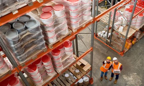 Warehouse workers navigating tall shelves stocked with construction materials in a well-organized industrial facility.